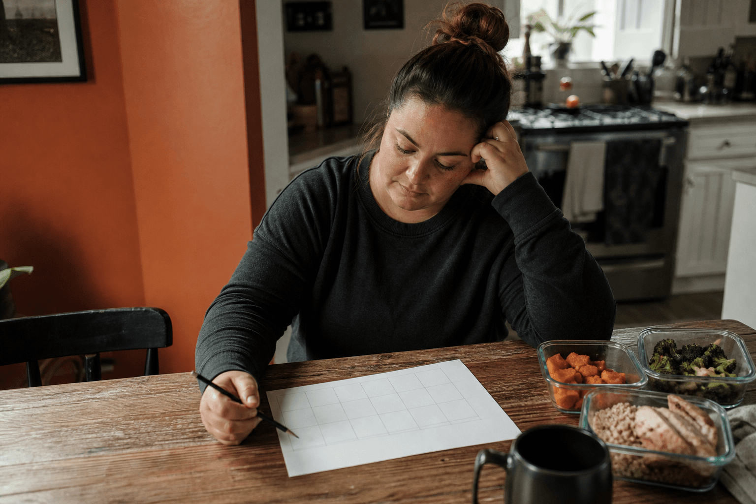 Adult reviewing a blank weekly plan beside simple meal prep in a home kitchen