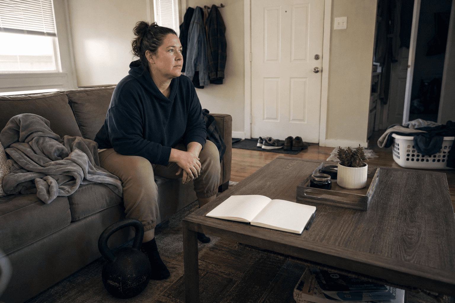Adult reviewing a blank notebook beside a kettlebell in a lived-in apartment living room