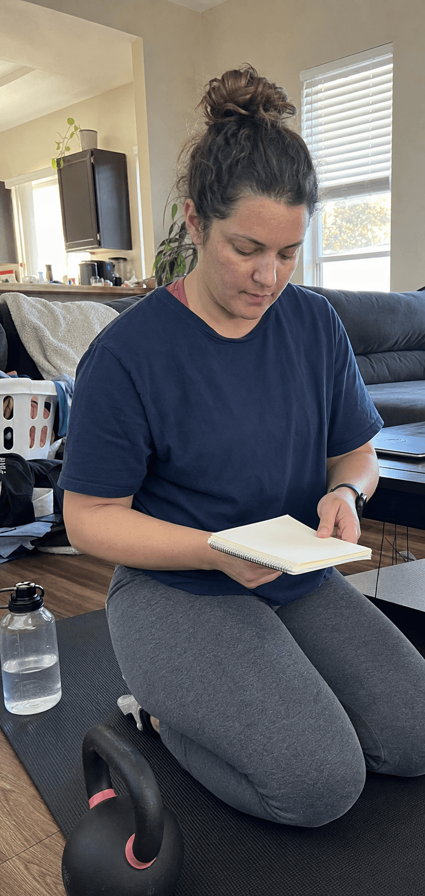 Adult reviewing a blank notebook beside a kettlebell in a lived-in apartment