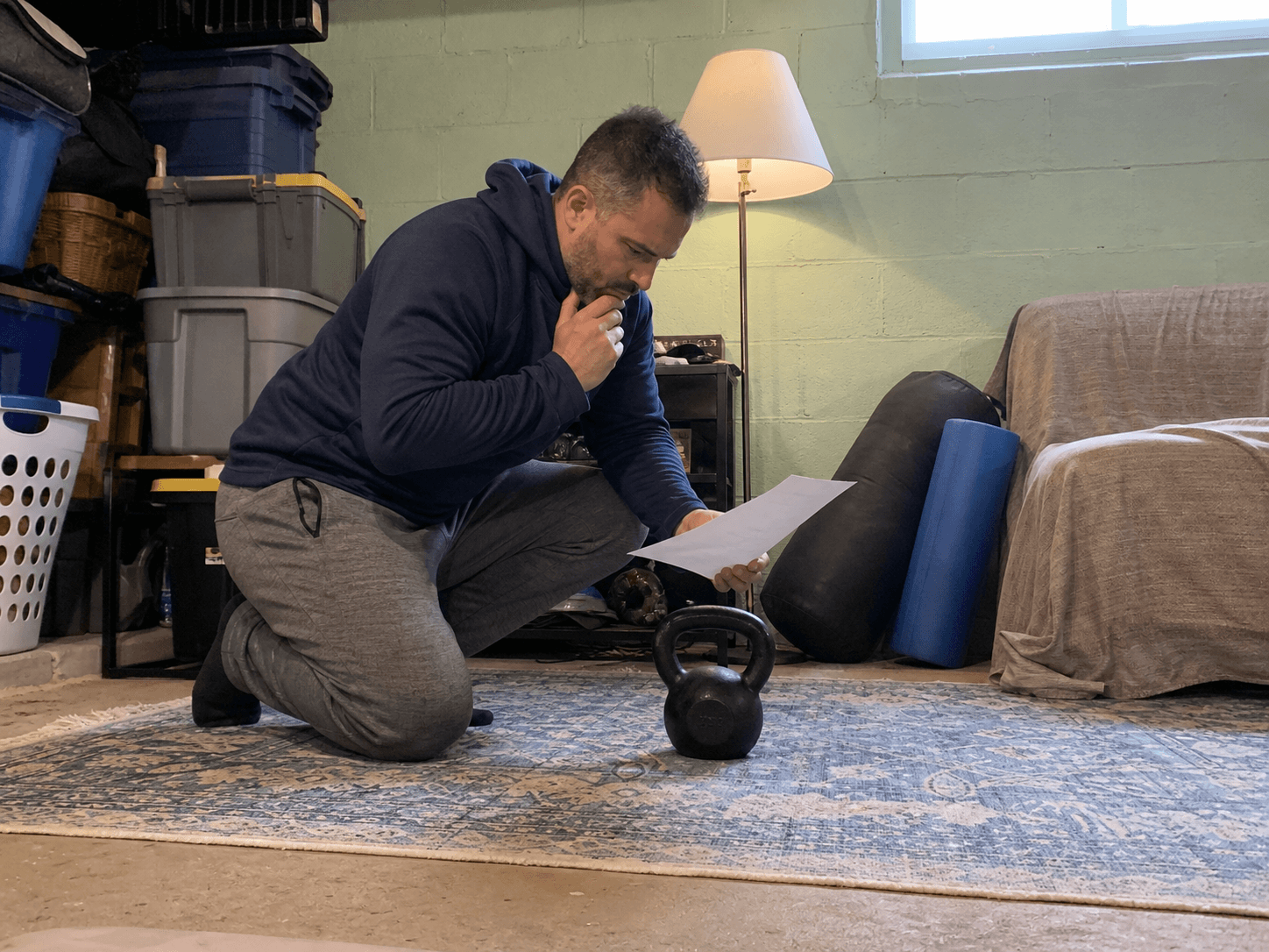 Adult reviewing a blank checklist beside a kettlebell in a lived-in basement training corner