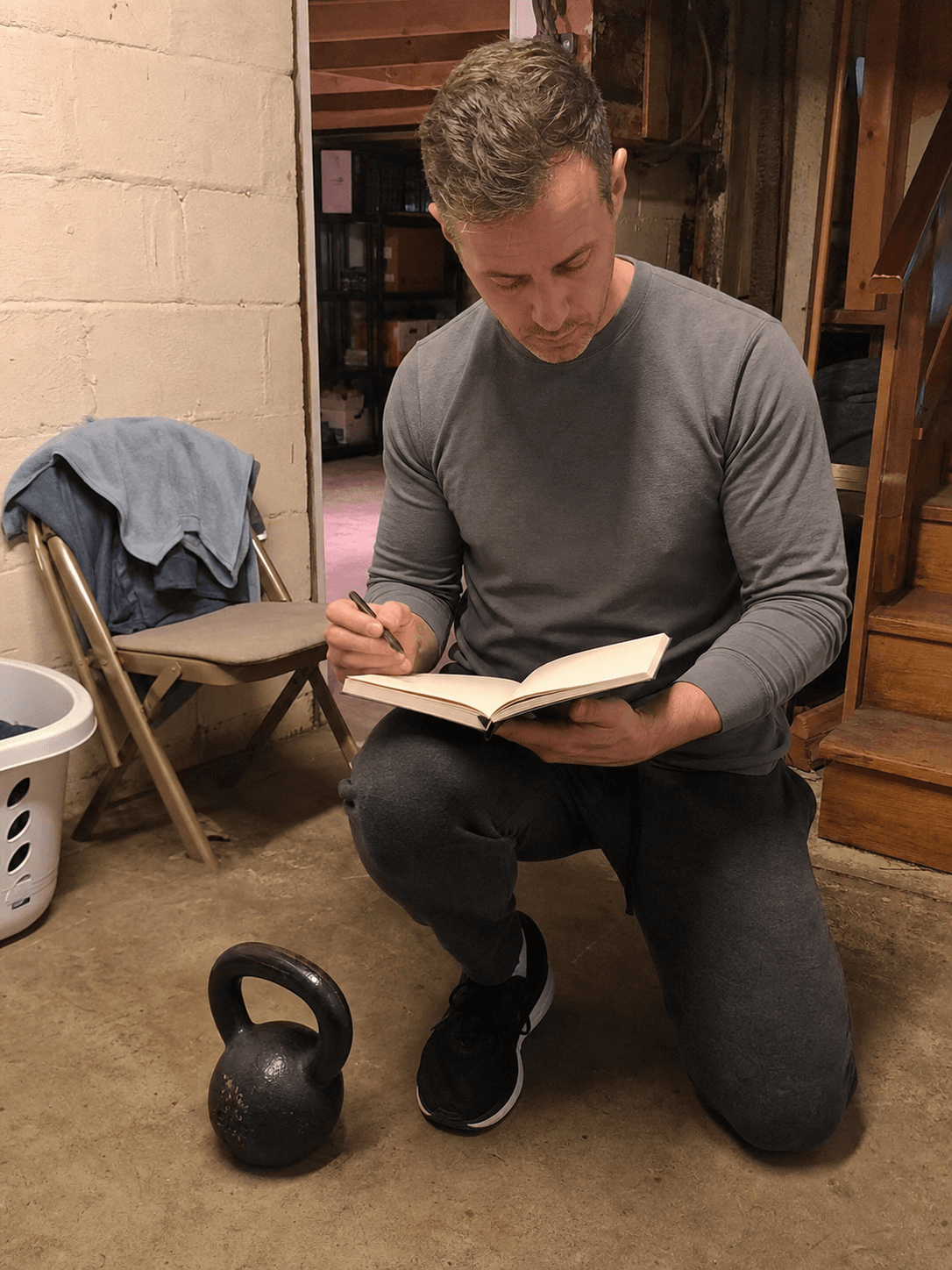 Adult reviewing a blank notebook beside a kettlebell in a basement training corner