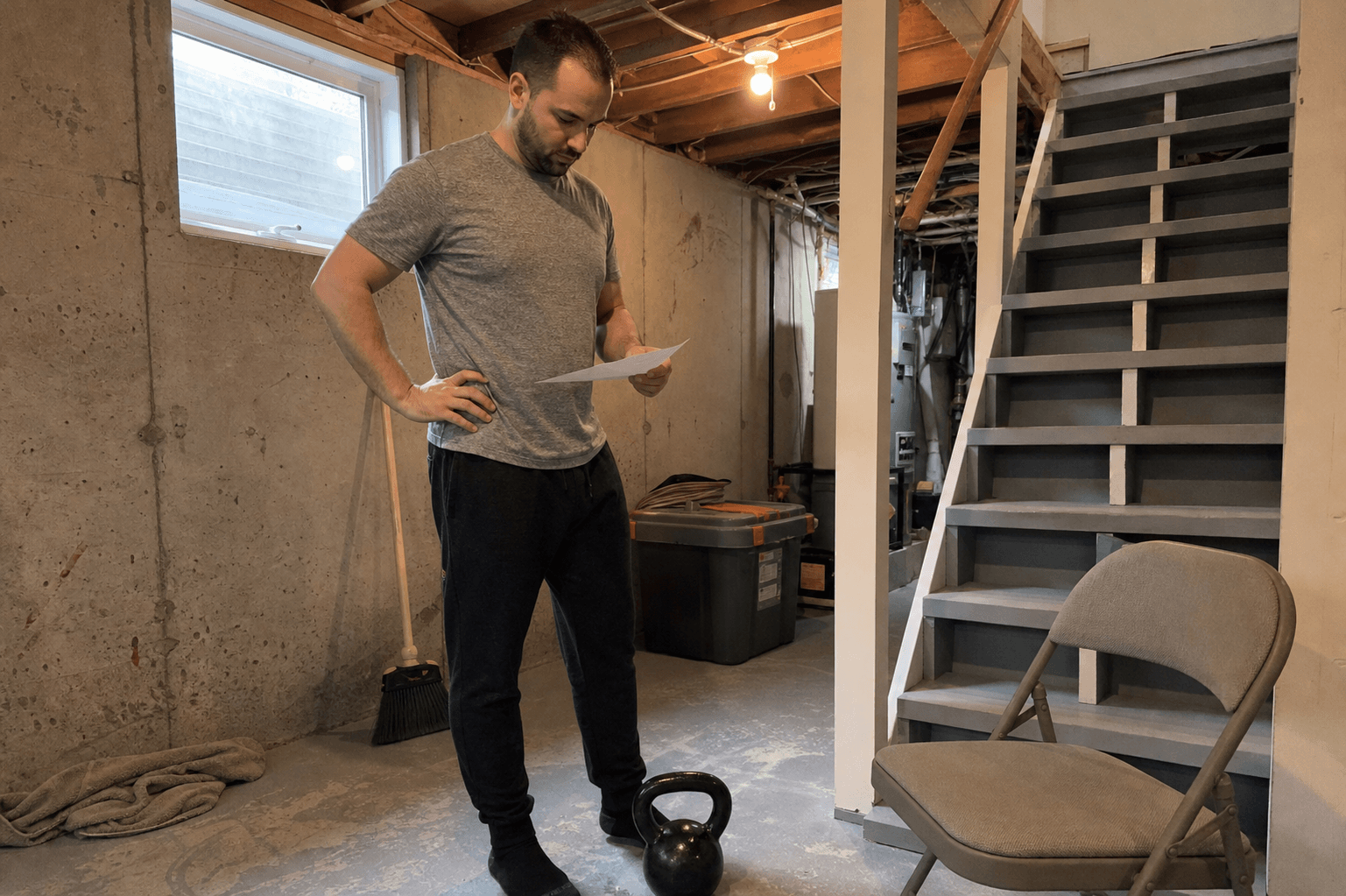 Adult reviewing blank training paper beside a kettlebell on a basement stair landing