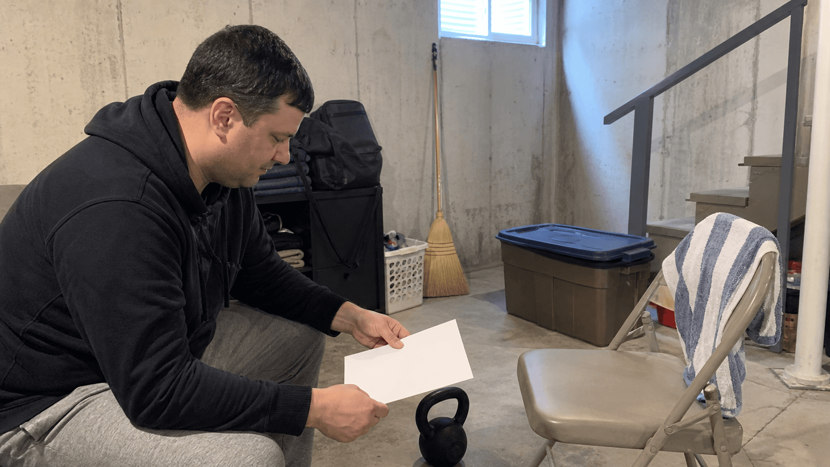 Adult reviewing blank training paper beside a kettlebell in a basement utility corner