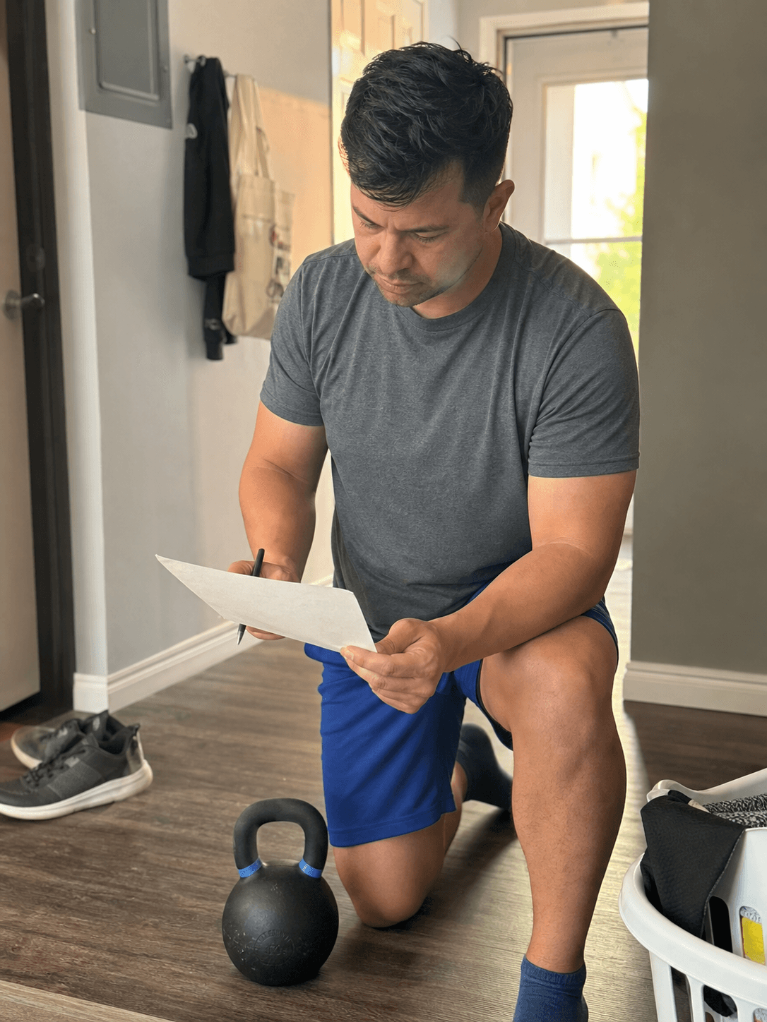 Adult reviewing a blank training checklist beside a kettlebell in a lived-in hallway utility corner