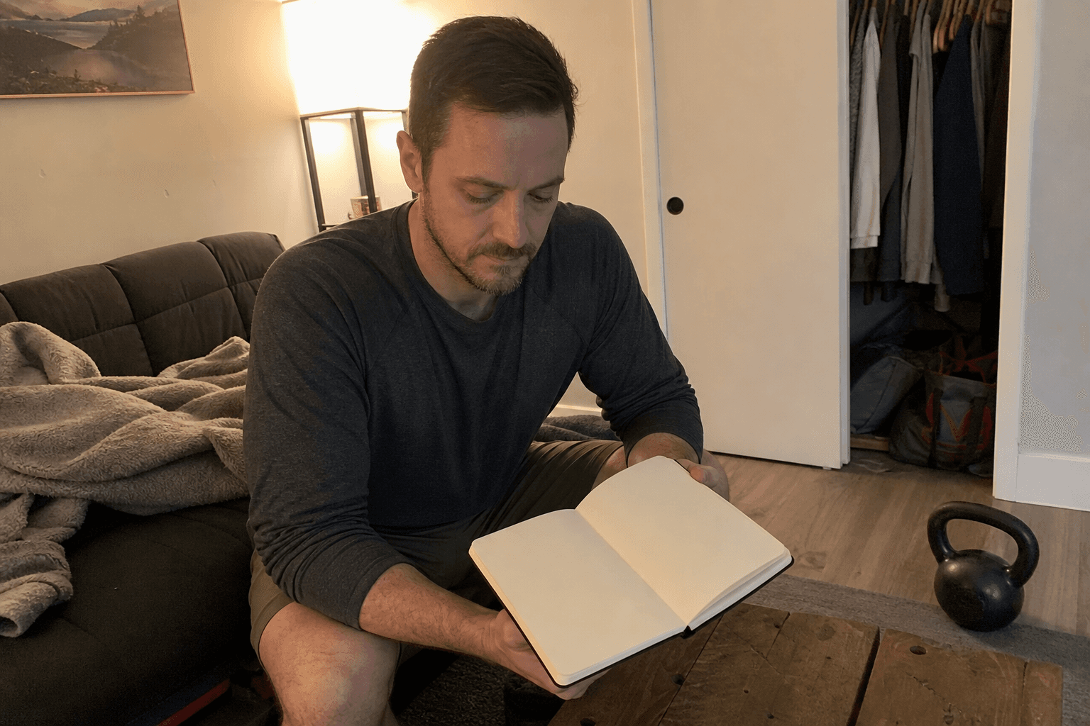Adult reviewing a blank notebook beside a kettlebell in a lived-in spare room