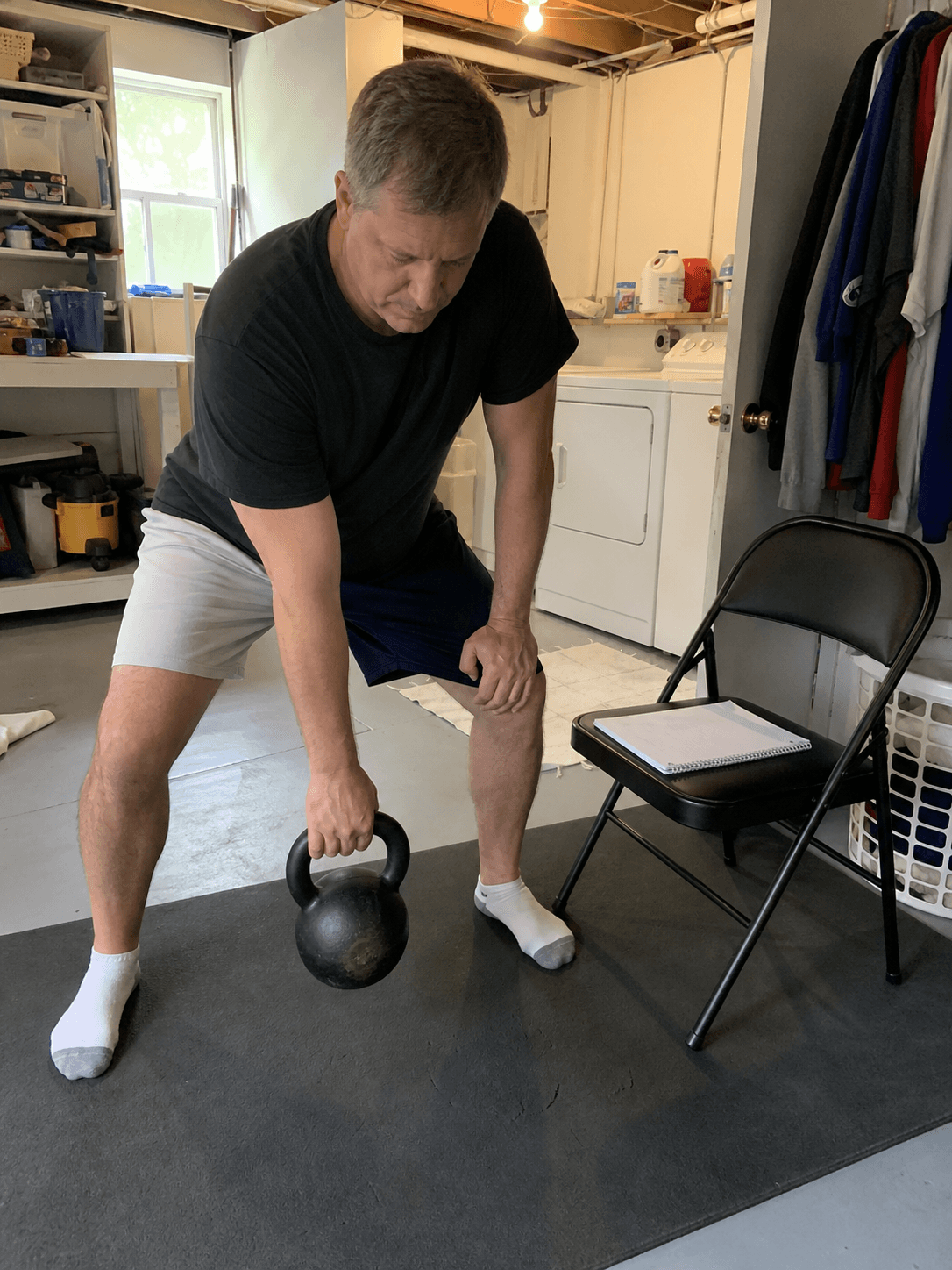 Adult checking a kettlebell session plan in a lived-in utility room