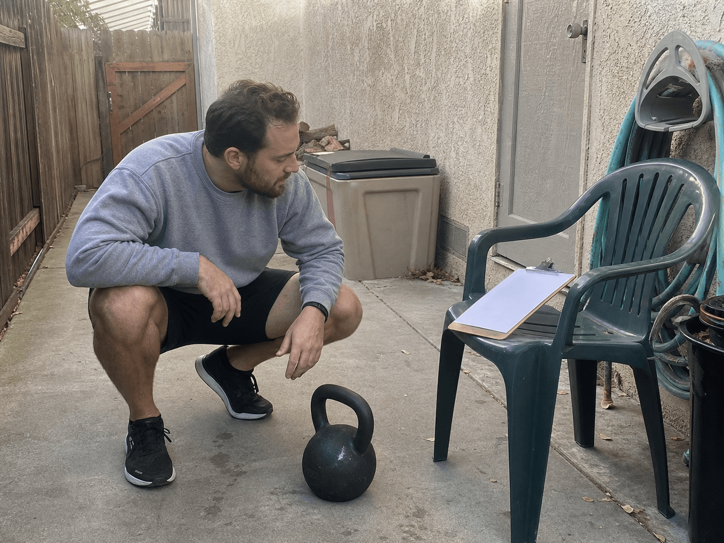 Adult reviewing a blank training check-in beside a kettlebell on a backyard patio