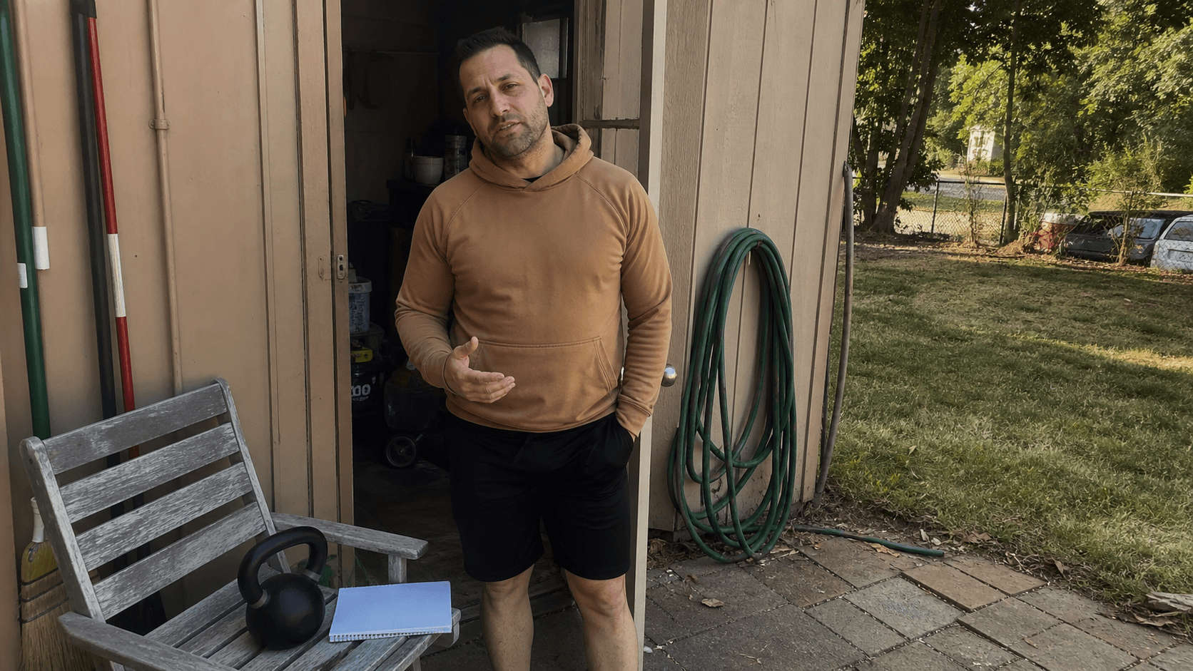 Adult reviewing a blank training check-in beside a kettlebell near a backyard shed doorway