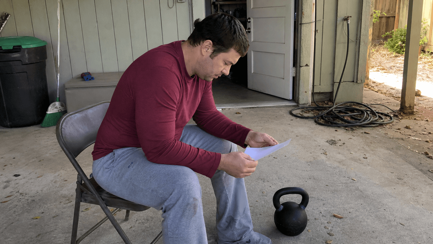 Adult reviewing a blank training paper beside a kettlebell at a carport side entrance
