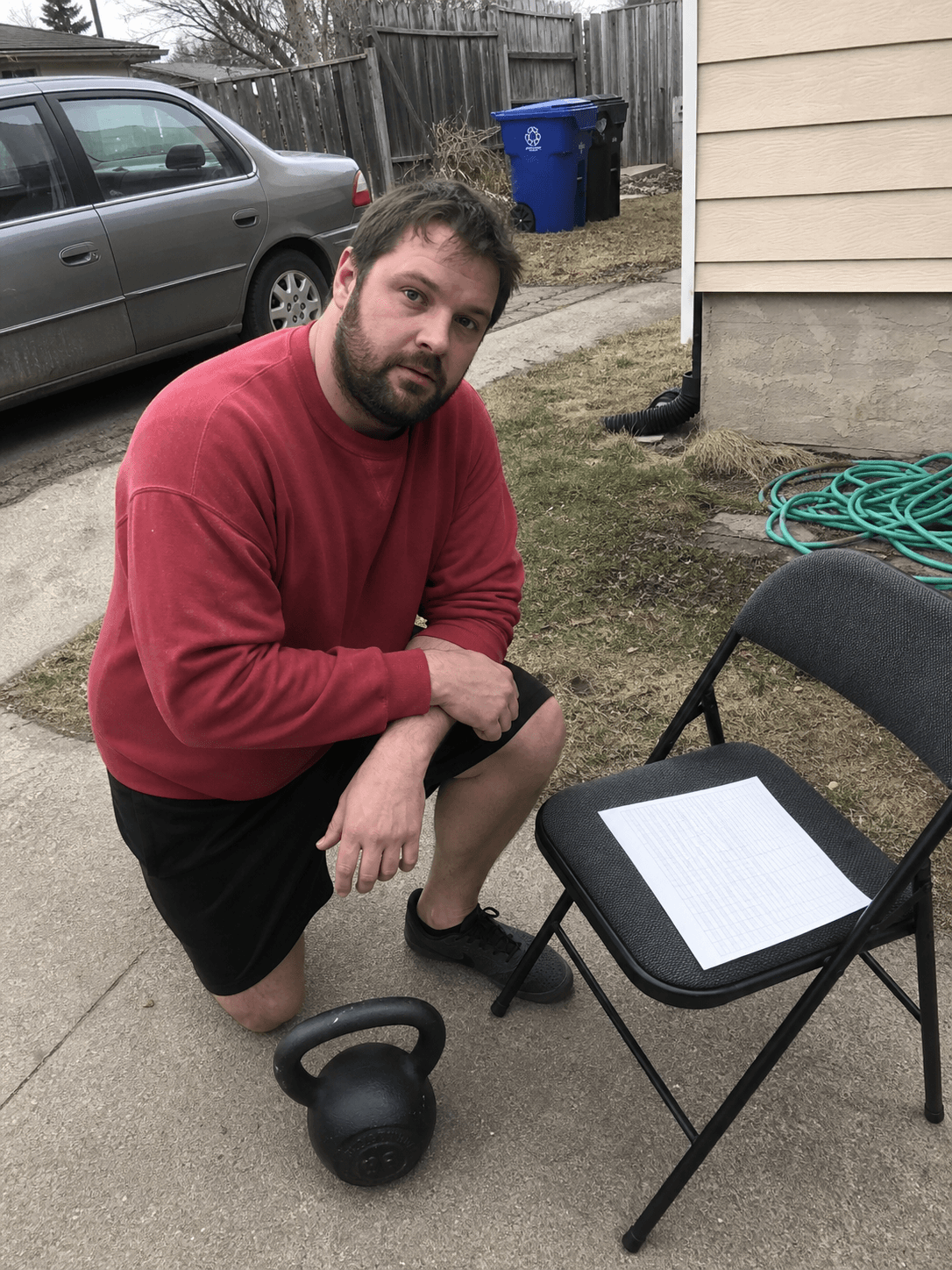 Adult reviewing a blank training check-in beside a kettlebell in a driveway side yard