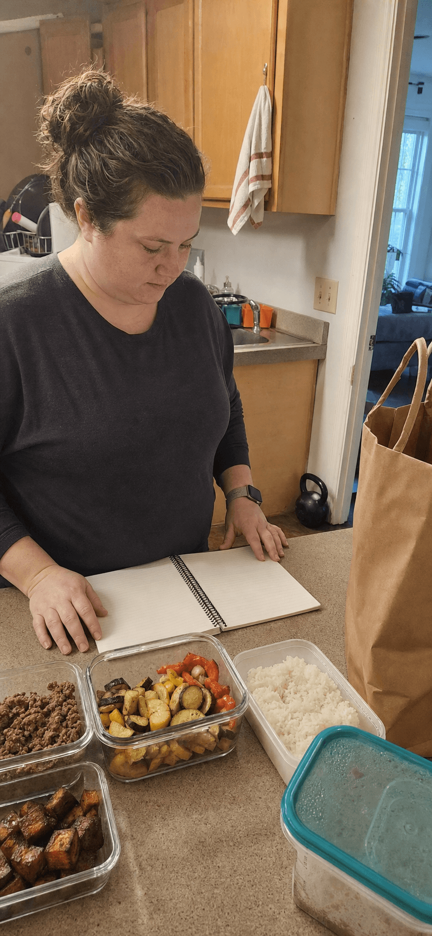 Adult reviewing a blank notebook beside simple meal prep in a small kitchen